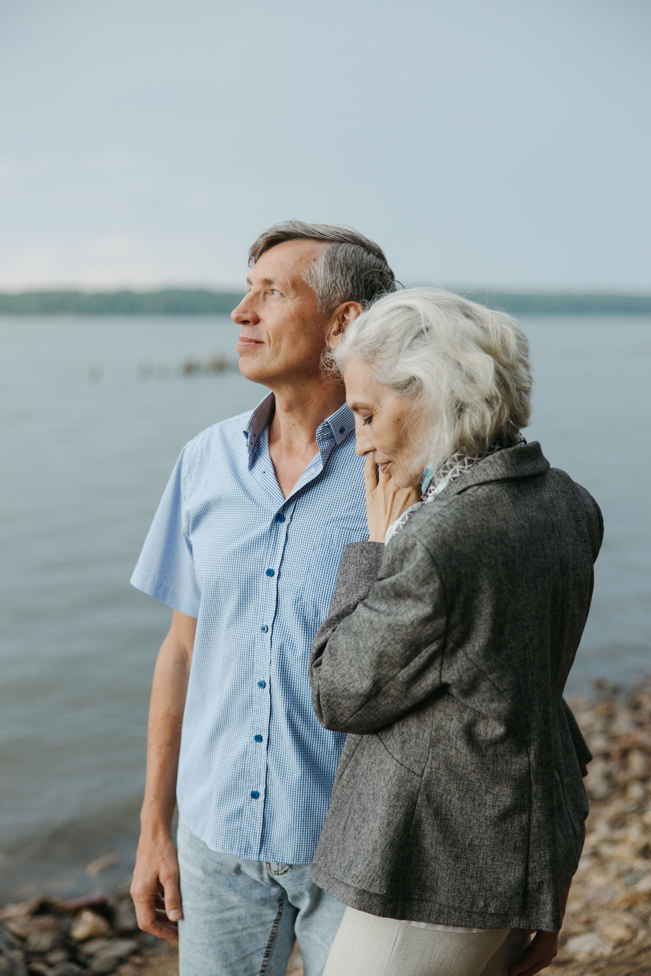 Silver-haired couple standing together looking out over a calm lake