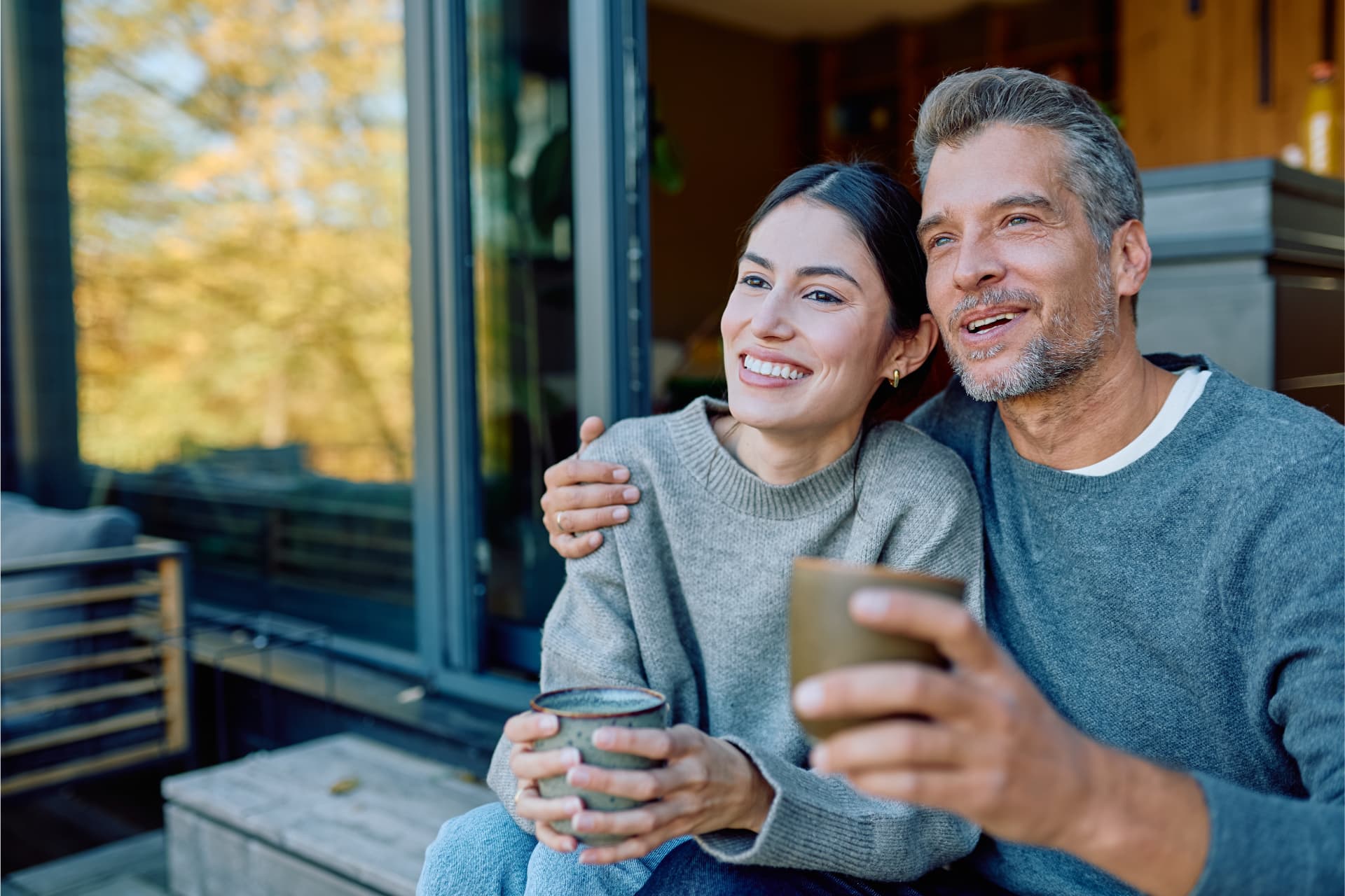 A smiling couple relaxing together with coffee outside their home