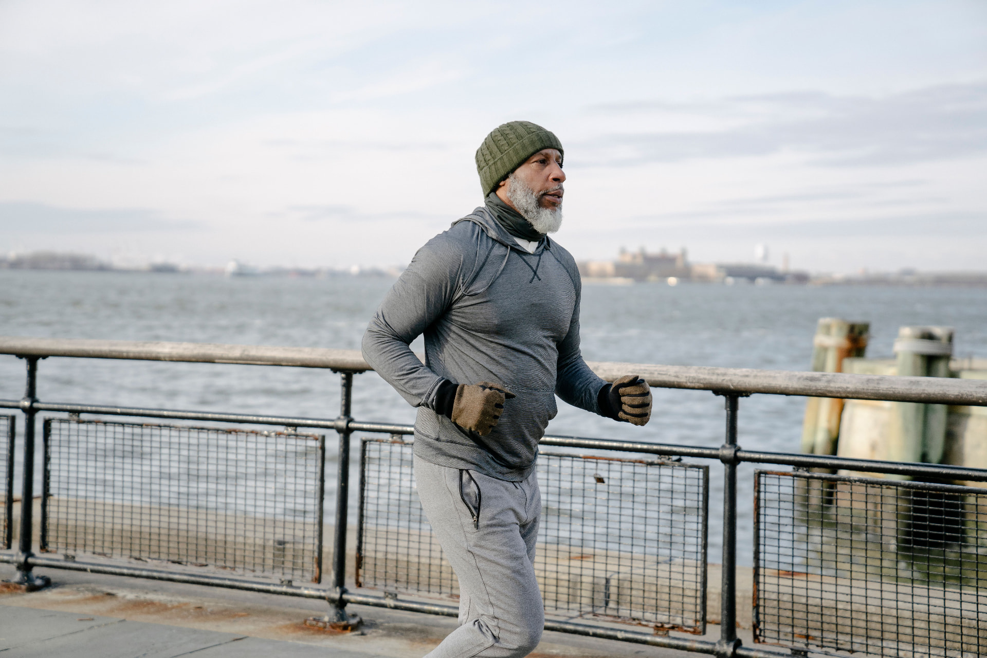 Older man running along a waterfront path in cold weather