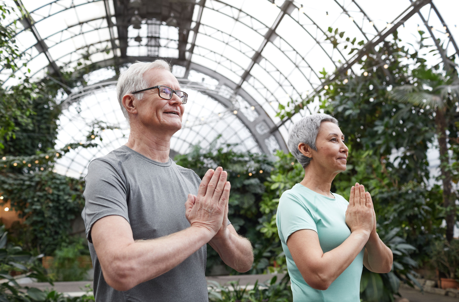 Older couple practising yoga together in a bright glasshouse